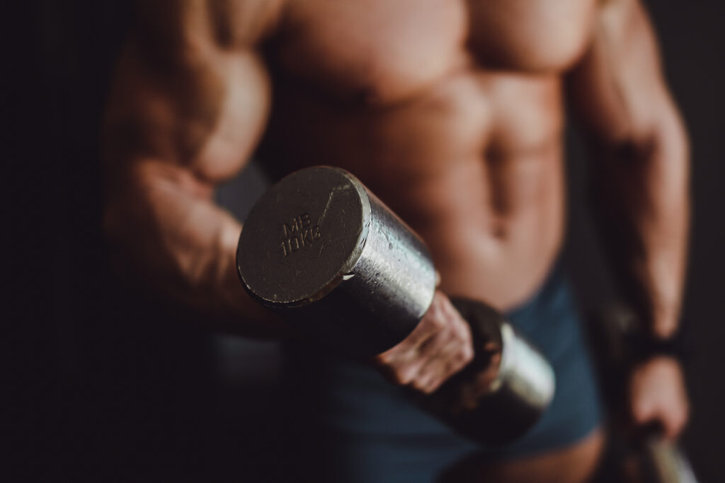 Atleta musculoso levantando halteres, representando os efeitos do Whey Protein no ganho de massa muscular e recuperação.