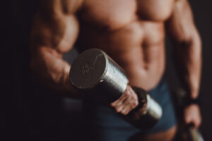 Atleta musculoso levantando halteres, representando os efeitos do Whey Protein no ganho de massa muscular e recuperação.